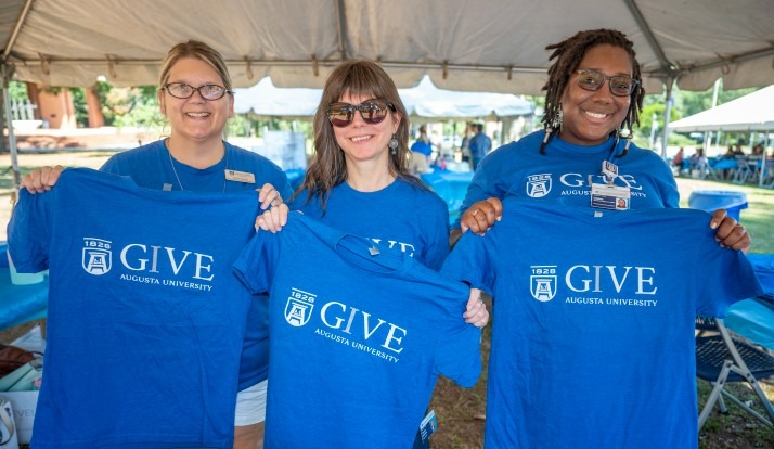 three ladies hold up IGIVE t-shirts