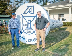 two men stand with golf tee sculpture