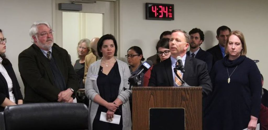 Frank Lomonte stands at a microphone with several other people listening nearby