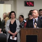 Frank Lomonte stands at a microphone with several other people listening nearby