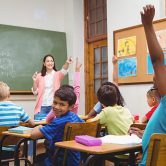 A teacher in a classroom calls on elementary school students.