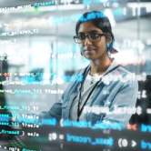 A cybersecurity analyst works at a desktop computer in a large office, with the running code superimposed in the foreground.