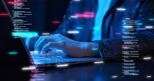 The hands of a cybersecurity professional work a keyboard to display lines of code, which are suspended in space around his laptop.
