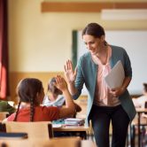A smiling classroom teacher high fives a sitting student.