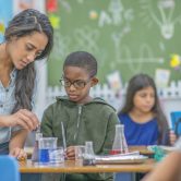 A teacher helping an elementary school child with a chemistry experiment in the classroom.