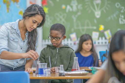 A teacher helping an elementary school child with a chemistry experiment in the classroom.