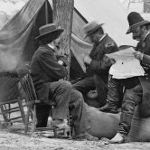 Black and white historical photo of Civil War soldiers reading a newspaper