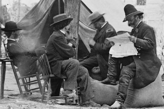 Black and white historical photo of Civil War soldiers reading a newspaper