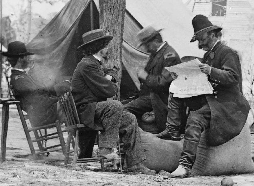 Black and white historical photo of Civil War soldiers reading a newspaper