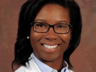 Headshot in white coat on brown background of Dr. Ashley Nunnally