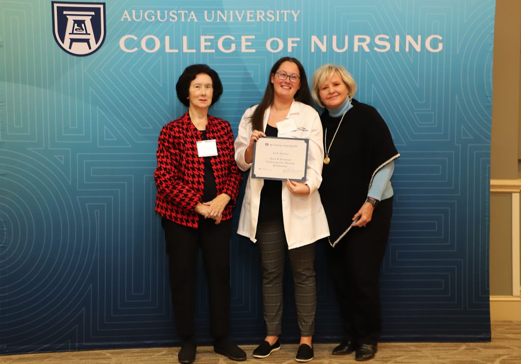 Three women stand next to each other and smile for a photo while one holds a certificate.