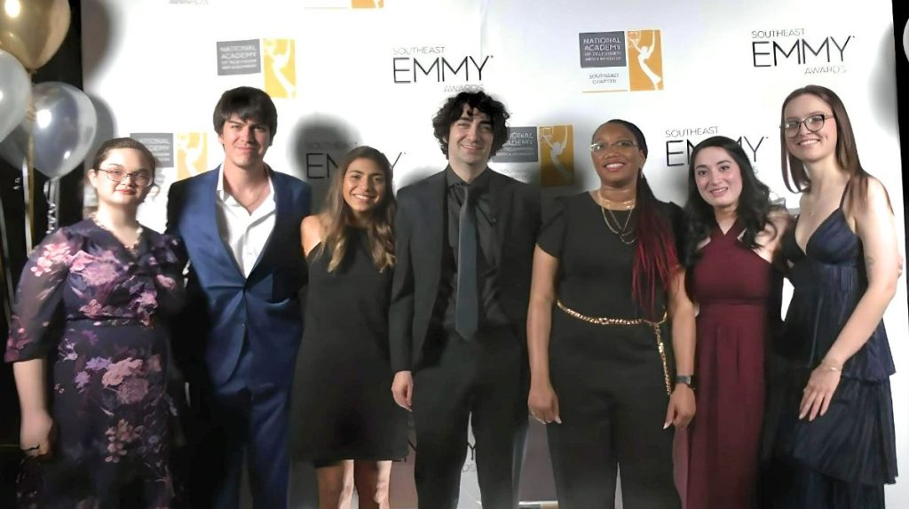 Shows a group of Augusta University students in front of an Emmy sign at awards ceremony
