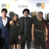 Shows a group of Augusta University students in front of an Emmy sign at awards ceremony