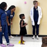 Local child is guided through eye test by Nurse Practitioner students