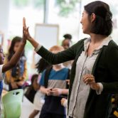 A teacher high fives a student in a classroom.