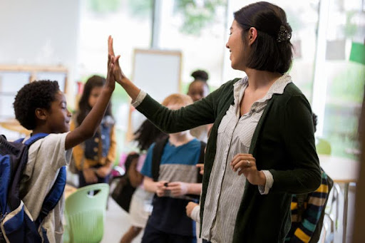 A teacher high fives a student in a classroom.