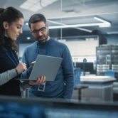 Two information security professionals standing in a server room, looking at a computer.