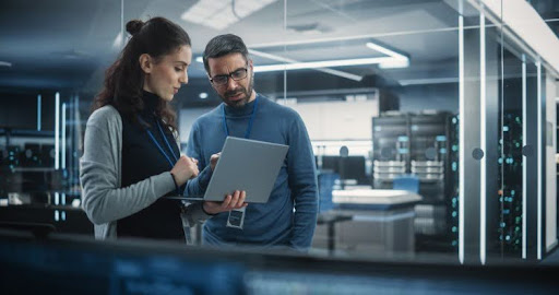 Two information security professionals standing in a server room, looking at a computer.