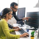 Two digital forensic examiners review code on a monitor.