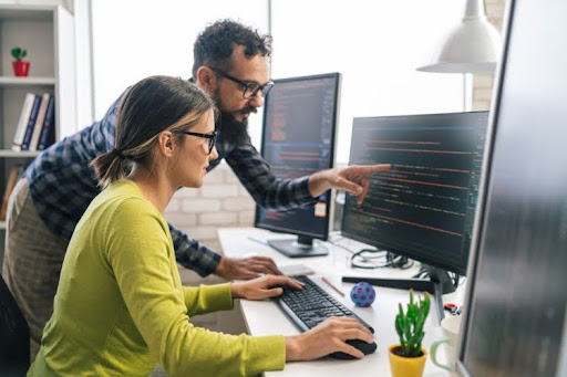 Two digital forensic examiners review code on a monitor.