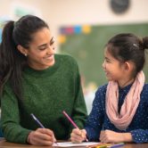 A smiling teacher sitting next to a student.