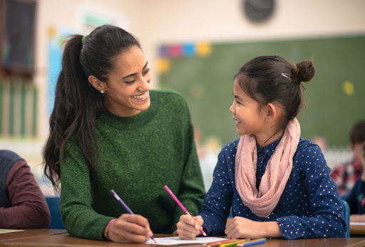 A smiling teacher sitting next to a student.