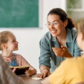 A smiling teacher talks to students in class.