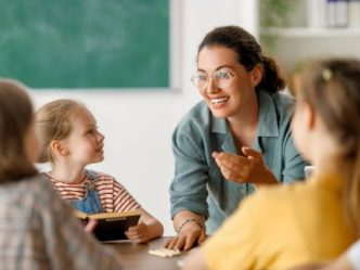 A smiling teacher talks to students in class.