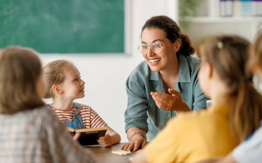 A smiling teacher talks to students in class.