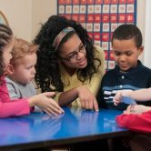 A teacher sits at a table with a group of young students.