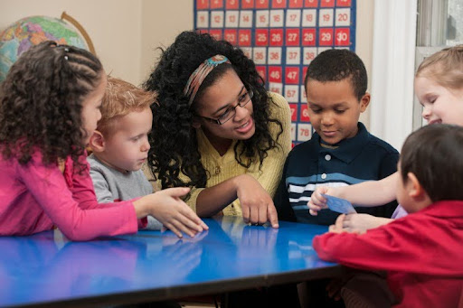 A teacher sits at a table with a group of young students.