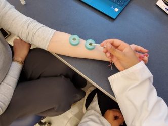 A person's outstretched arm with essential oils being administered by student in white coat