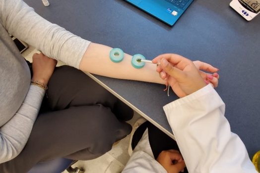 A person's outstretched arm with essential oils being administered by student in white coat