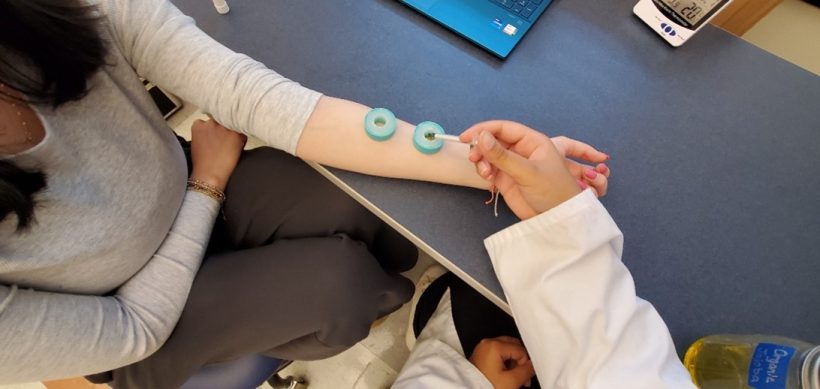 A person's outstretched arm with essential oils being administered by student in white coat