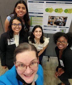 Dr. Dawn Langley-Brady poses with her students in front of a project poster