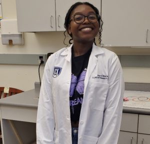 Student Brandi Bramwell smiling in a lab coat