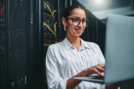 A security architect working on a laptop in a server room.