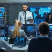 A cybersecurity manager speaks to a team of analysts in a control room.