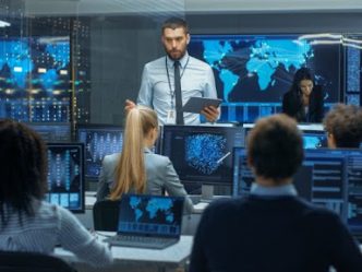 A cybersecurity manager speaks to a team of analysts in a control room.