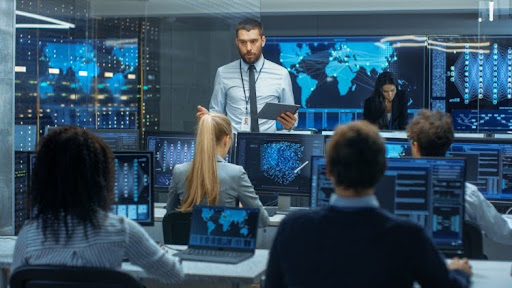 A cybersecurity manager speaks to a team of analysts in a control room.