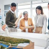 A team of urban planners look at a blueprint and a city model.