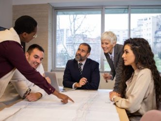 A city manager points to a map during a council meeting around a conference table.