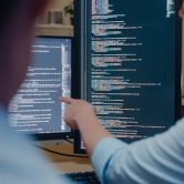 A cybersecurity manager points to an employee’s code on a monitor.