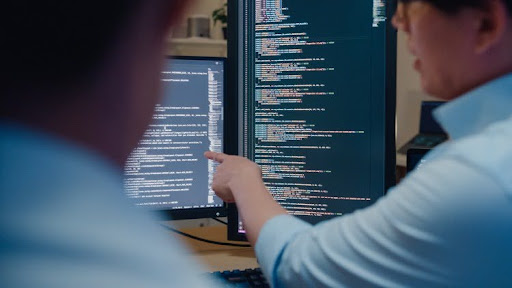 A cybersecurity manager points to an employee’s code on a monitor.