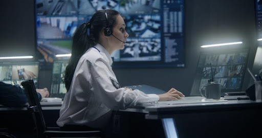 An immigration security officer wearing a headset watches surveillance footage on a computer.