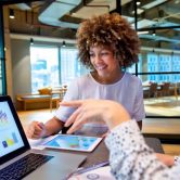 Two budget analysts meet and go over data on a laptop and tablet.