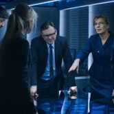 A team of counterintelligence officers meeting in a conference room stand around a digital touch screen table.