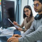 Two cybersecurity professionals look at a computer monitor and analyze code.