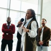 A fundraising manager holding a microphone delivers a funding pitch to potential donors.