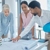 Three urban planners work with blueprints and a 3D model of a construction project.